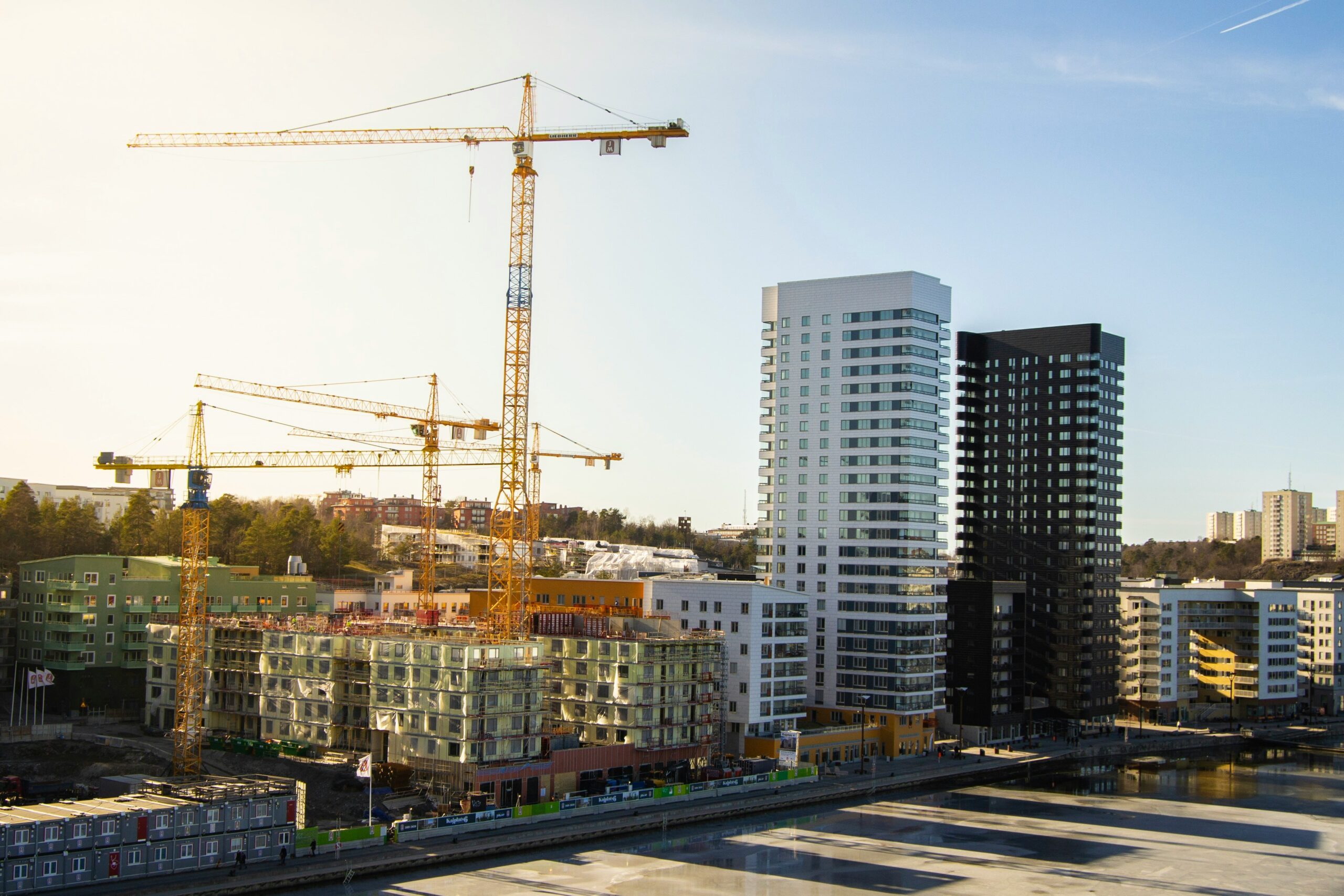A drone with four propellers flies over a construction site with unfinished buildings and heavy machinery, showcasing drone technology in construction.