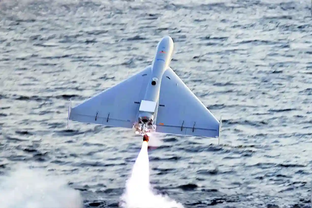 A Shahed-136 kamikaze drone flying at a very low altitude over an industrial power plant complex.