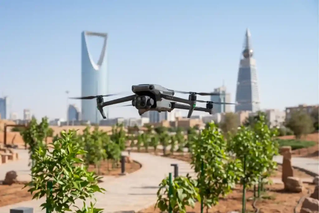 A compact DJI Mavic 3 Multispectral drone hovering over a newly planted green park path in Riyadh during a bright summer day.