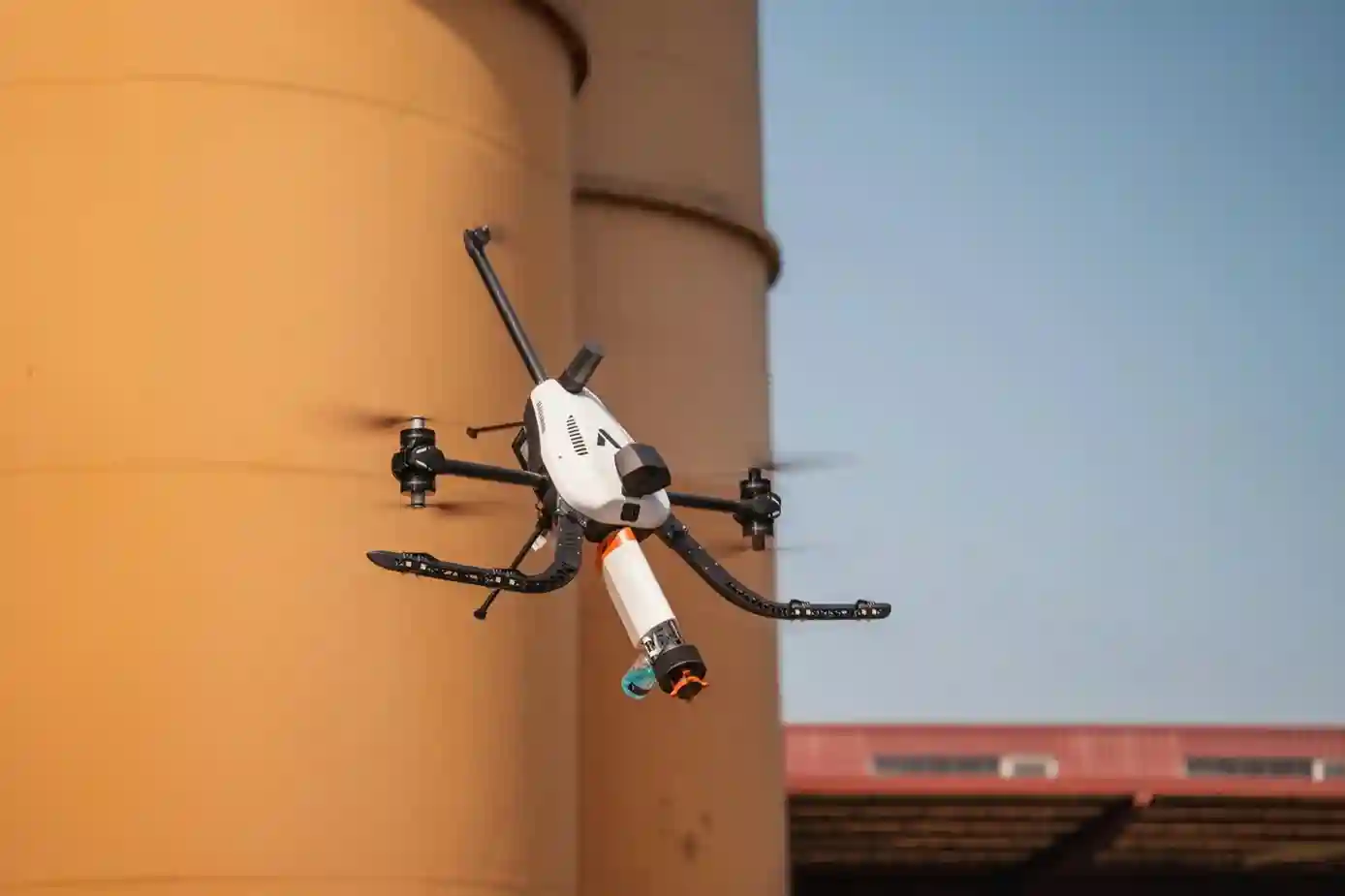Voliro T NDT drone pressing an acoustic ultrasonic probe against an elevated steel pressure vessel wall for thickness measurement.