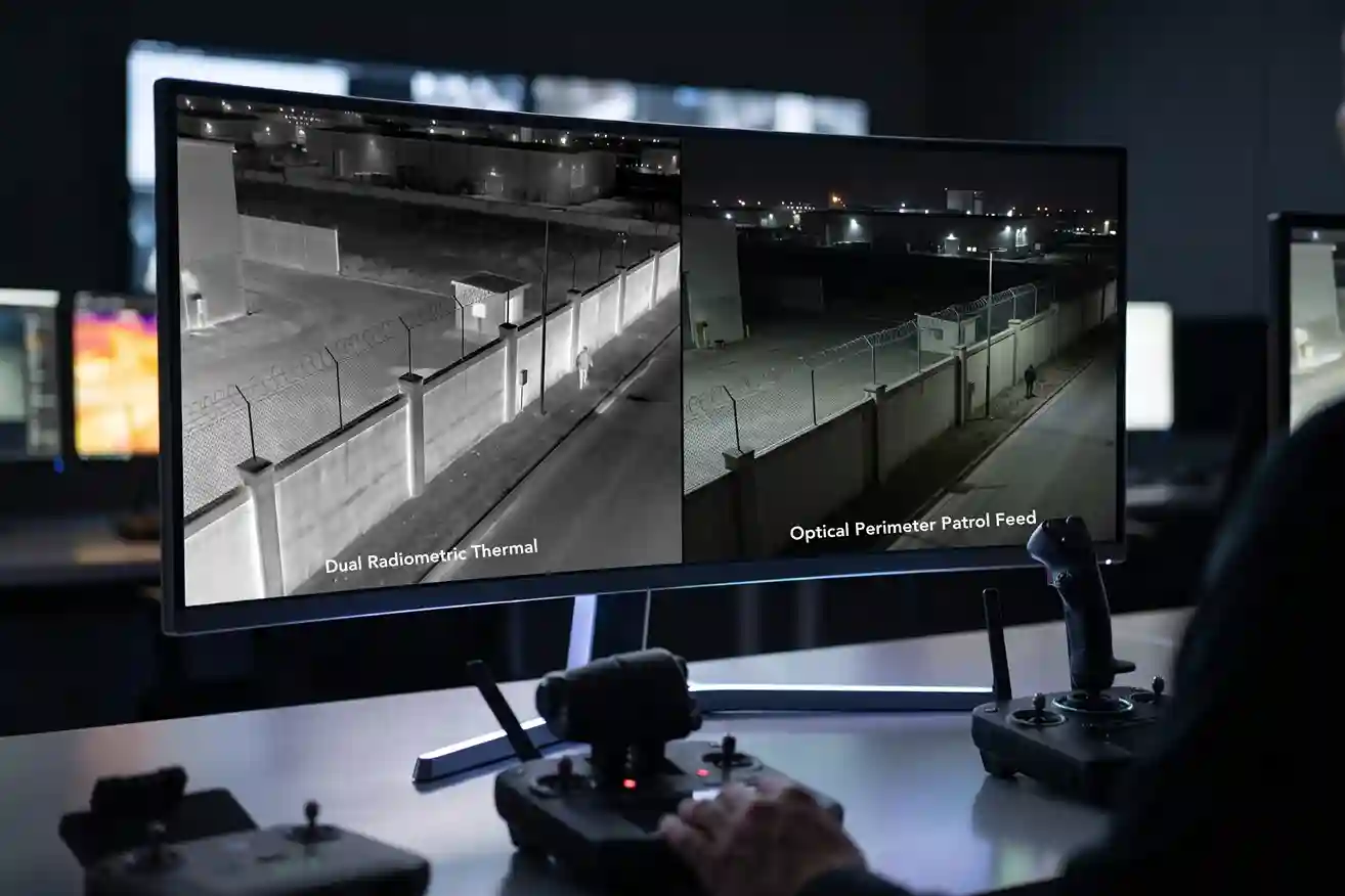 Split-screen thermal and optical video feed of an industrial park perimeter fence line captured during a night drone patrol.